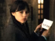 Jenna ortega s wednesday looking curiously over her shoulder while holding a note in wednesday season